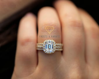 May include: A gold engagement ring with a large emerald cut diamond center stone surrounded by a halo of smaller diamonds. The ring is set on a band with two smaller diamond bands on either side.
