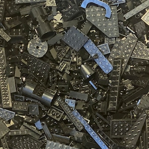 May include: A large pile of black Lego bricks of various shapes and sizes. The bricks are all made of plastic and have a smooth, glossy finish.