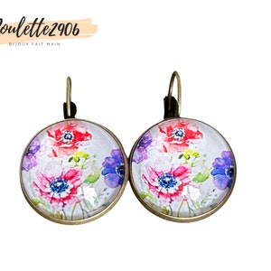 Op de afbeelding: Een paar ronde oorbellen met een bloemenontwerp. De oorbellen hebben een print in aquarel-stijl van rode, roze en paarse bloemen met groene bladeren. De oorbellen hebben een bronskleurig metalen frame en oorhaaksluitingen. De tekst "Poulette2906 BIJOUX FAIT MAIN" staat in de linkerbovenhoek.
