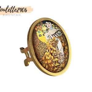 Op de afbeelding: Verstelbare ring in goudkleur met een ovaal ontwerp met een print van een beroemd schilderij. De ring heeft een gedetailleerde afbeelding van een vrouw in een gouden en gele jurk. De tekst "Poulette2906 BIJOUX FAIT MAIN" is zichtbaar linksboven.