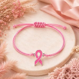 Peut inclure: Un bracelet en cordon rose avec une breloque en métal argenté en forme de ruban de sensibilisation, doté d'un émail rose. Le bracelet est muni d'un fermoir coulissant réglable fabriqué dans le même cordon rose que la bande principale.