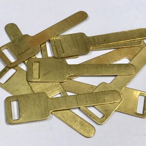 May include: A pile of small, brass-coloured metal components. Each piece has a rectangular form with a key-like design, including a rectangular opening at one end and a broader section at the other.