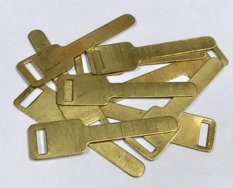 May include: A pile of small, brass-coloured metal components. Each piece has a rectangular form with a key-like design, including a rectangular opening at one end and a broader section at the other.