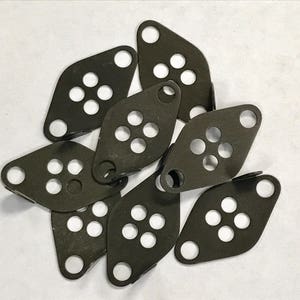 May include: A collection of dark gray metal plates with rounded edges and multiple circular holes. Each plate has a single hole for mounting. The plates are arranged on a white surface.