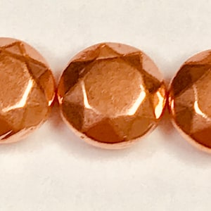 May include: Three copper-colored, faceted, round beads. Each bead has a geometric design with multiple flat surfaces that reflect light. The beads are arranged in a horizontal line against a white background. These beads are suitable for jewelry making.