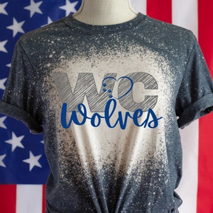 May include: A dark gray t-shirt with a white splatter design. The shirt has a graphic print of the letters "WC" with a heart in the middle and the word "Wolves" underneath.