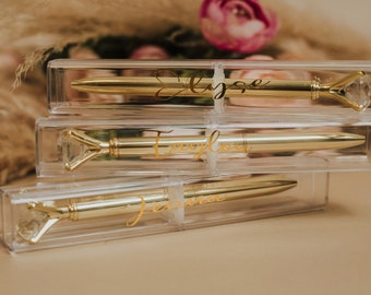May include: Three clear acrylic boxes stacked on top of each other. Each box contains a gold pen with a diamond-shaped top. The pens are personalized with the names "Elyse", "Evelyn", and "Jennifer".