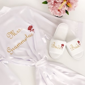 May include: White satin robe with gold embroidery that says "Mrs. Grammalas" and a red rose. Two white slippers with gold embroidery that says "Bride" and a red rose.