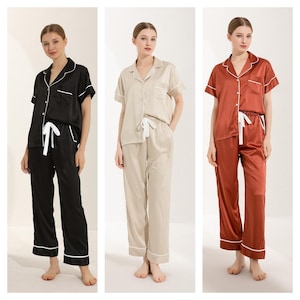 Könnte beinhalten: Drei Damen-Pyjama-Sets in Schwarz, Beige und Rost. Jedes Set besteht aus einem kurzärmeligen, geknöpften Oberteil mit weißem Besatz und einer passenden Hose mit Kordelzug und weißem Besatz.
