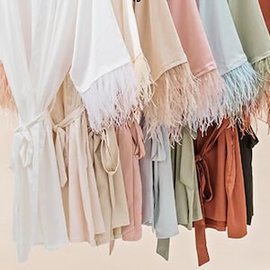 May include: A collection of silky robes with feather trim on the sleeves. The robes are in various colors, including white, beige, pink, blue, green, and brown.