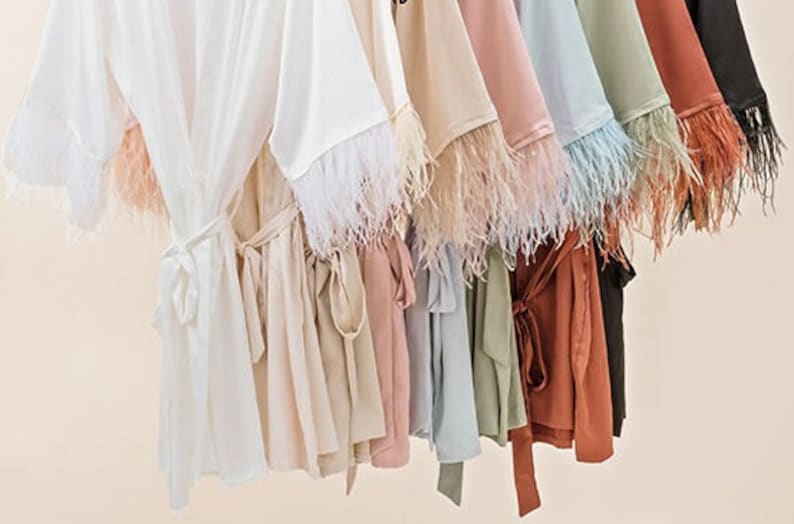 May include: A collection of silky robes with feather trim on the sleeves. The robes are in various colors, including white, beige, pink, blue, green, and brown.