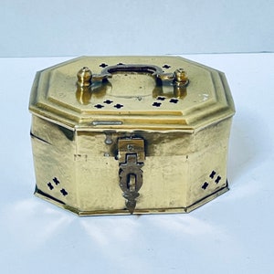 May include: A brass octagonal box with a hinged lid and a decorative latch. The box has a handle on the top and is decorated with small holes.