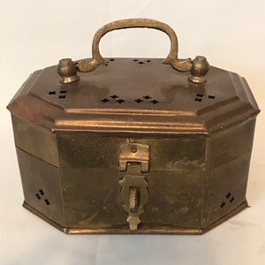 May include: A vintage brass box with an octagonal shape, featuring a handle and decorative perforations. The box has a clasp closure and small decorative knobs on the top. The brass has a warm, aged patina.