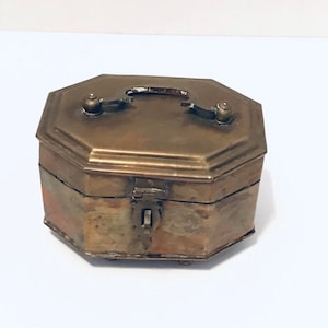May include: Octagonal brass box with a hinged lid and a handle on top. The box has a worn, antique finish and a small lock on the front.