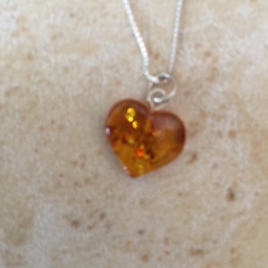 May include: A silver chain necklace with a heart-shaped amber pendant. The amber is a warm, honey colour with flecks of gold.