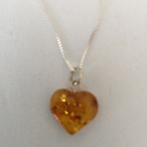 May include: A silver chain necklace with a heart-shaped amber pendant. The amber is a warm, honey colour with flecks of gold.