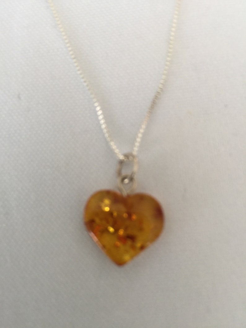 May include: A silver chain necklace with a heart-shaped amber pendant. The amber is a warm, honey colour with flecks of gold.