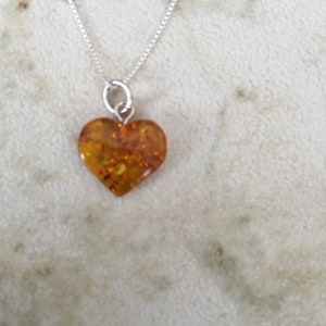May include: A silver chain necklace with a heart-shaped amber pendant. The amber is a warm, honey colour with flecks of gold.