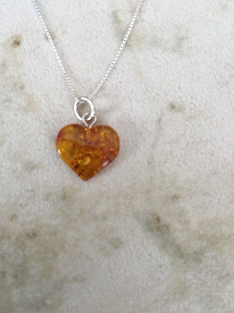 May include: A silver chain necklace with a heart-shaped amber pendant. The amber is a warm, honey colour with flecks of gold.