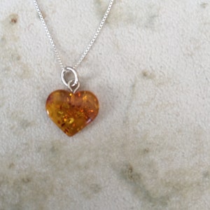 May include: A silver chain necklace with a heart-shaped amber pendant. The amber is a warm, honey colour with flecks of gold.