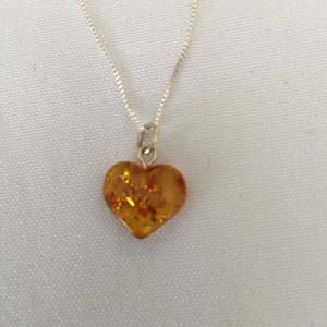 May include: A silver chain necklace with a heart-shaped amber pendant.