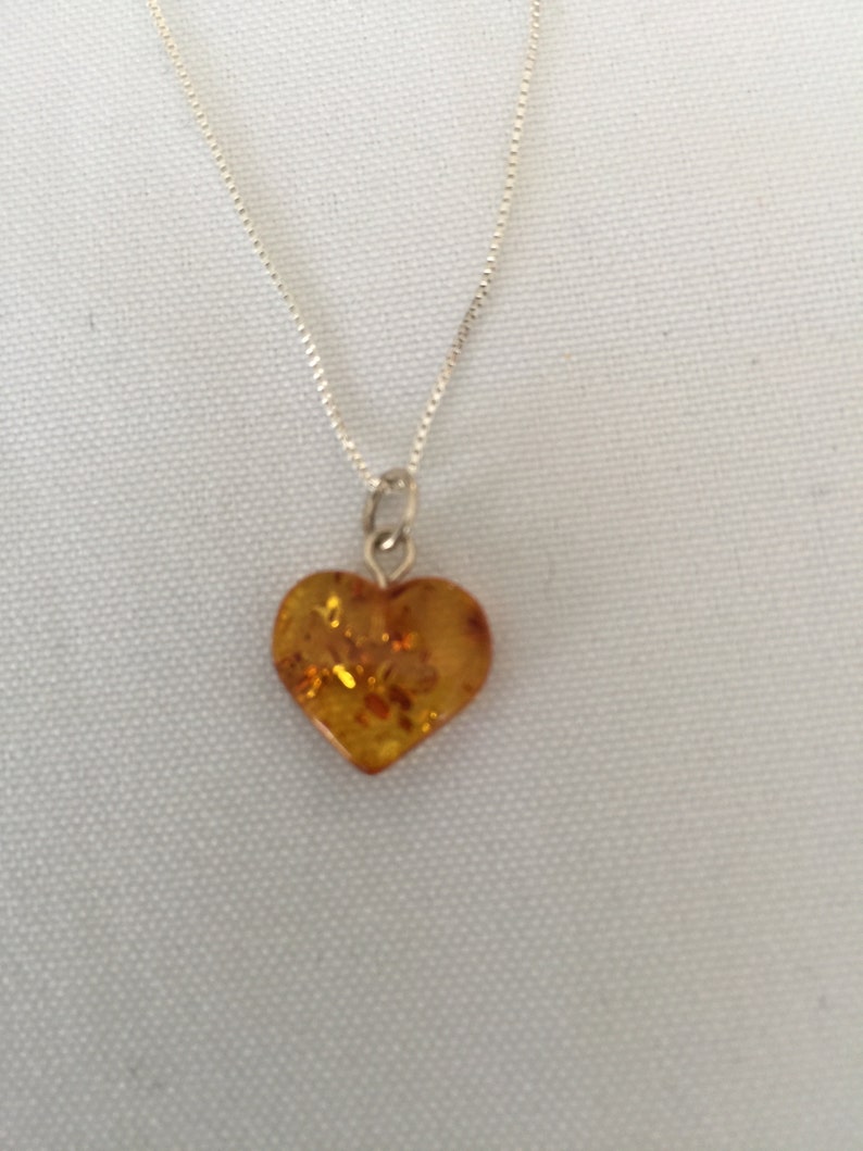 May include: A silver chain necklace with a heart-shaped amber pendant.