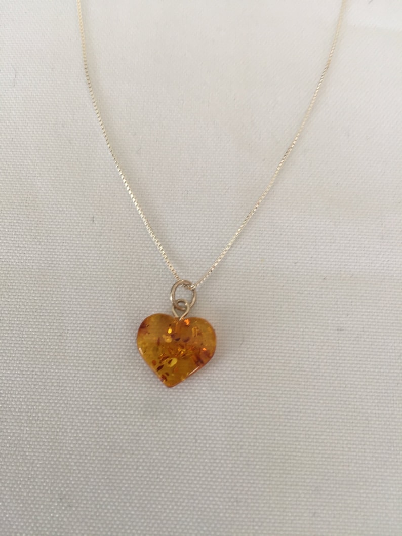 May include: A silver chain necklace with a heart-shaped amber pendant.