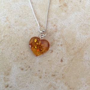 May include: A silver chain necklace with a heart-shaped amber pendant. The amber is a warm, honey colour with flecks of gold.