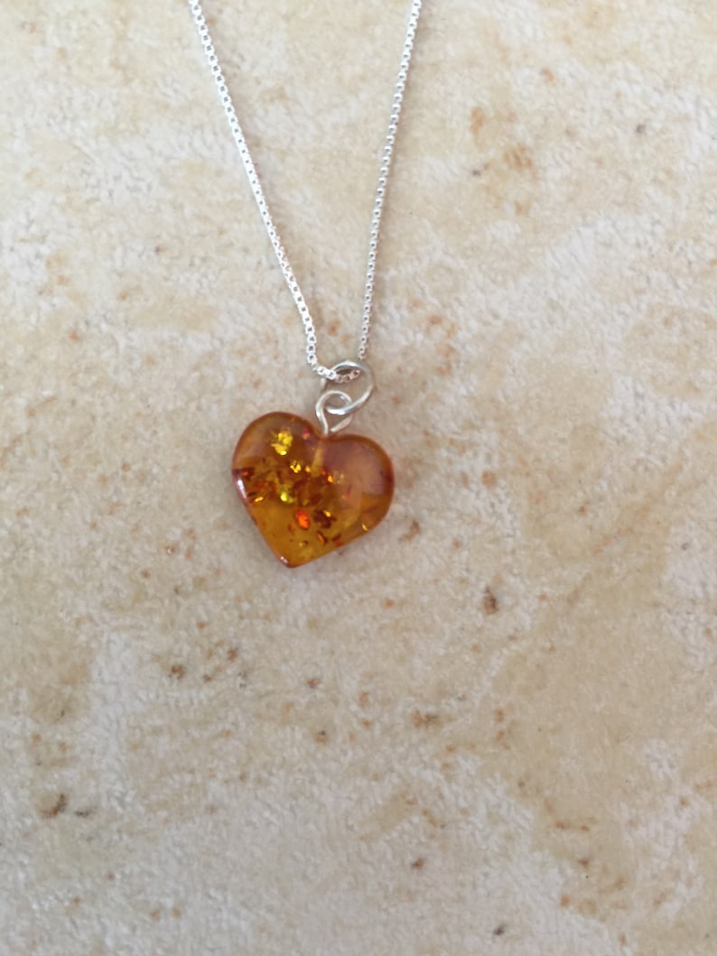 May include: A silver chain necklace with a heart-shaped amber pendant. The amber is a warm, honey colour with flecks of gold.