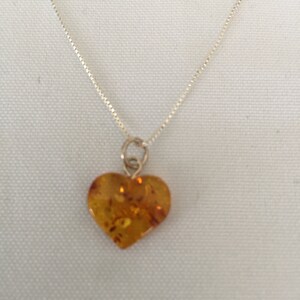 May include: A silver chain necklace with a heart-shaped amber pendant.