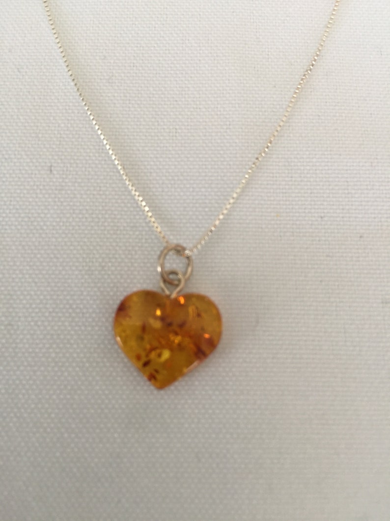 May include: A silver chain necklace with a heart-shaped amber pendant.