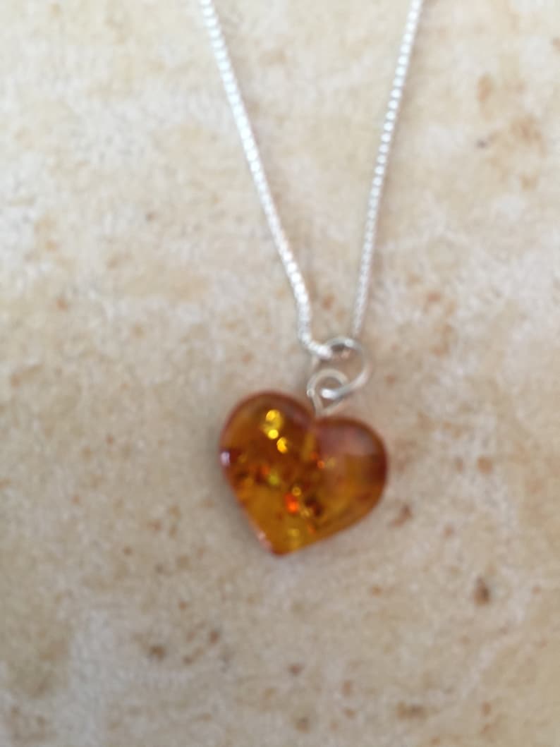 May include: A silver chain necklace with a heart-shaped amber pendant. The amber is a warm, honey colour with flecks of gold.