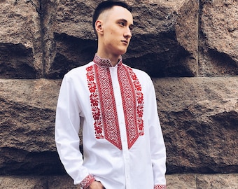 May include: A white long-sleeve shirt with intricate red embroidery on the collar, cuffs, and front. The shirt is paired with black jeans and white sneakers. The shirt's design is a traditional folk style.