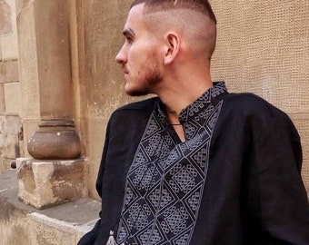 Peut inclure: Une chemise noire à manches longues avec un motif géométrique brodé blanc sur le devant. La chemise a un col en V et un détail de pompon sur le devant.