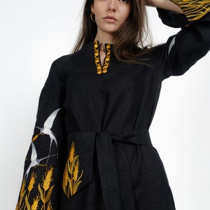May include: A black linen dress with embroidered white birds and yellow wheat stalks on the sleeves and neckline. The dress has a tie belt.