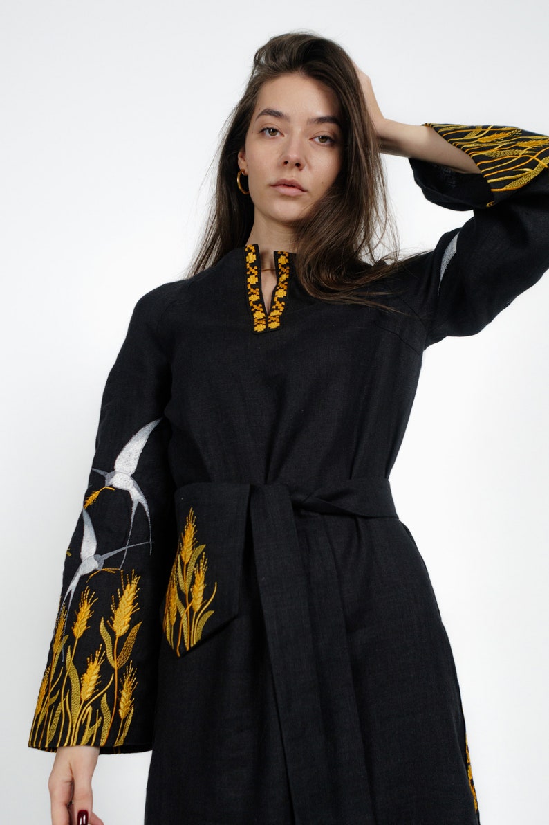 May include: A black linen dress with embroidered white birds and yellow wheat stalks on the sleeves and neckline. The dress has a tie belt.