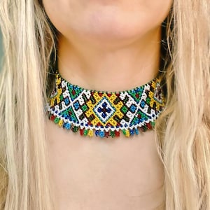 May include: A colorful beaded choker necklace with a geometric pattern. The necklace features a variety of colors including blue, green, yellow, red, and white. The choker has a fringe of small beads along the bottom edge.
