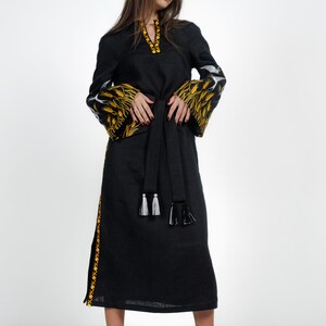 May include: A black linen dress with embroidered yellow and white floral patterns on the sleeves and a black sash with white tassels.