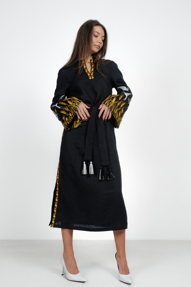 May include: A black linen dress with embroidered yellow and white floral patterns on the sleeves and a black sash with white tassels.