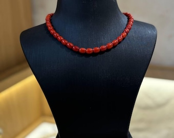 May include: A red coral bead necklace on a black display stand.