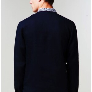 May include: A navy blue long-sleeved shirt with a white embroidered pattern around the collar and cuffs.