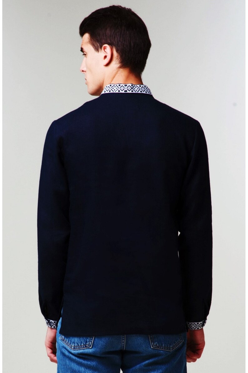 May include: A navy blue long-sleeved shirt with a white embroidered pattern around the collar and cuffs.