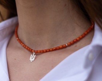 May include: A necklace made of orange beads with a silver trident pendant.