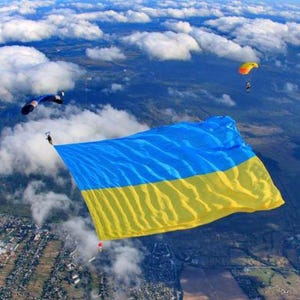 May include: A large Ukrainian flag is being flown by skydivers in the sky. The flag is blue and yellow and is being held by two people. The skydivers are wearing parachutes and are flying over a field of clouds.