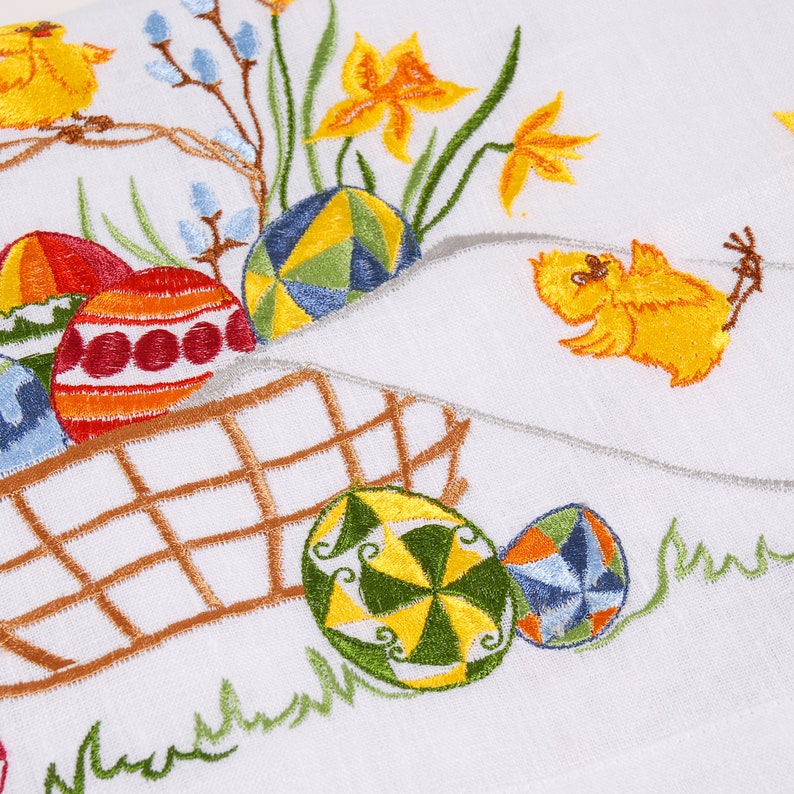 May include: Embroidered white kitchen towel featuring a basket of colourful Easter eggs, two yellow chicks, and spring flowers.
