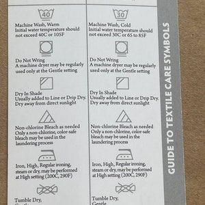 May include: A white card with black text and symbols outlining care instructions for white and coloured clothing. The card includes instructions for washing, drying, bleaching, ironing, and tumble drying. The card also includes the text "Guide to Textile Care Symbols".