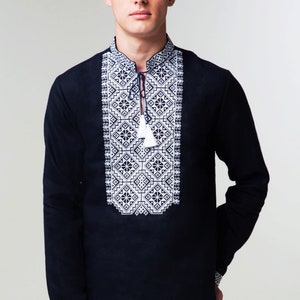 May include: A black long-sleeved shirt with a white embroidered geometric pattern on the front. The shirt has a stand-up collar and a button closure.
