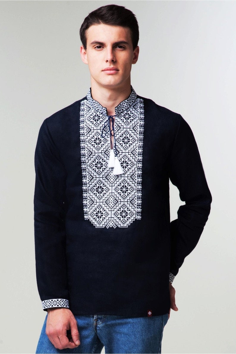 May include: A black long-sleeved shirt with white embroidered geometric patterns on the front. The shirt has a button-up collar and a tassel tie.