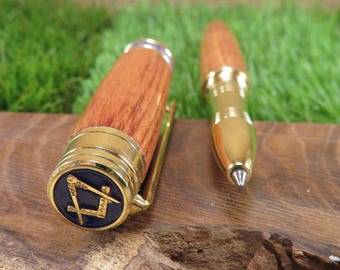 Könnte beinhalten: Ein Holzstift mit goldfarbenen Akzenten und einem Clip. Die Stiftkappe zeigt ein blaues Emblem mit einem goldenen Quadrat- und Zirkelsymbol. Der Stift besteht aus Holz mit sichtbarer Maserung.