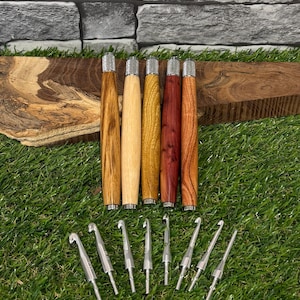 May include: A selection of crochet hooks with wooden handles in various shades of wood, and silver metal hooks. The hooks are displayed on a bed of green grass.